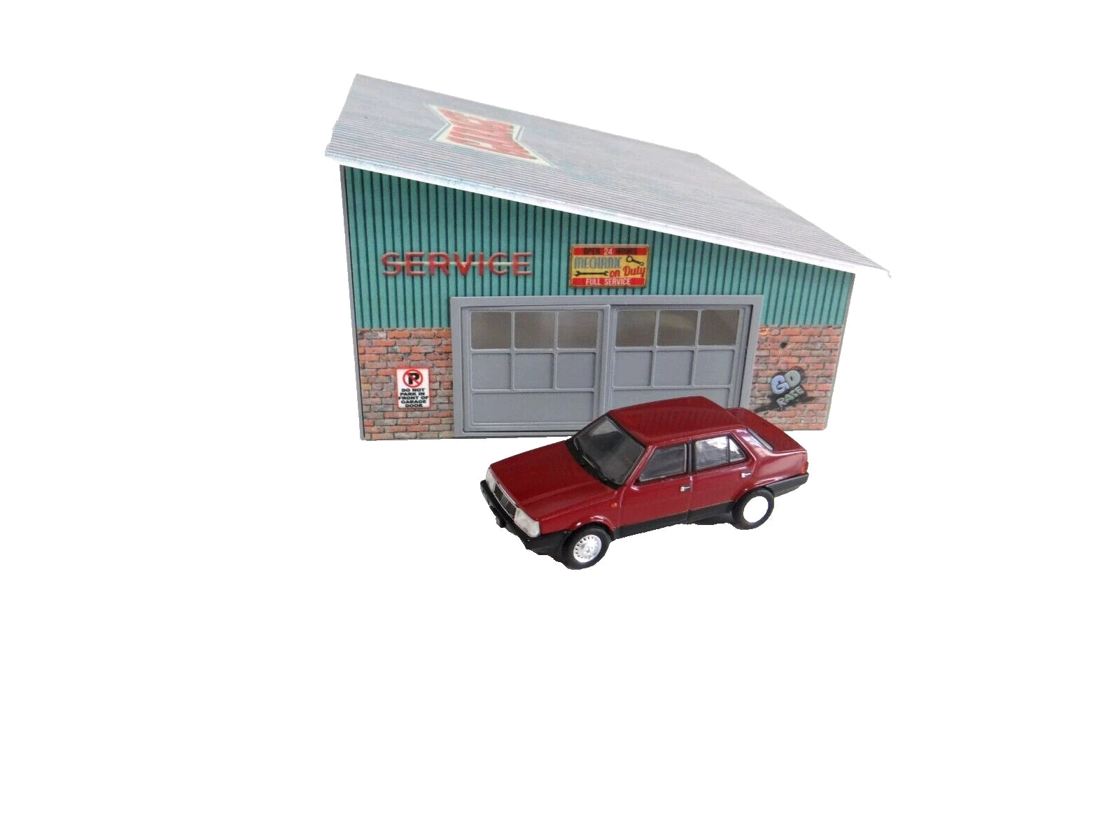 Model car in front of a miniature service station building on a white background