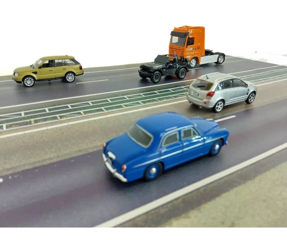 Model cars on a miniature road with different vehicles including a blue car, green SUV, and orange truck.